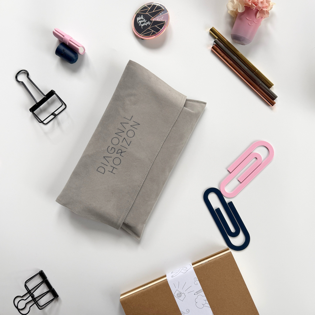 Gray fabric pouch with 'Diagonal Horizon' branding on a white surface with stationery items.