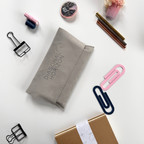 Gray fabric pouch with 'Diagonal Horizon' branding on a white surface with stationery items.