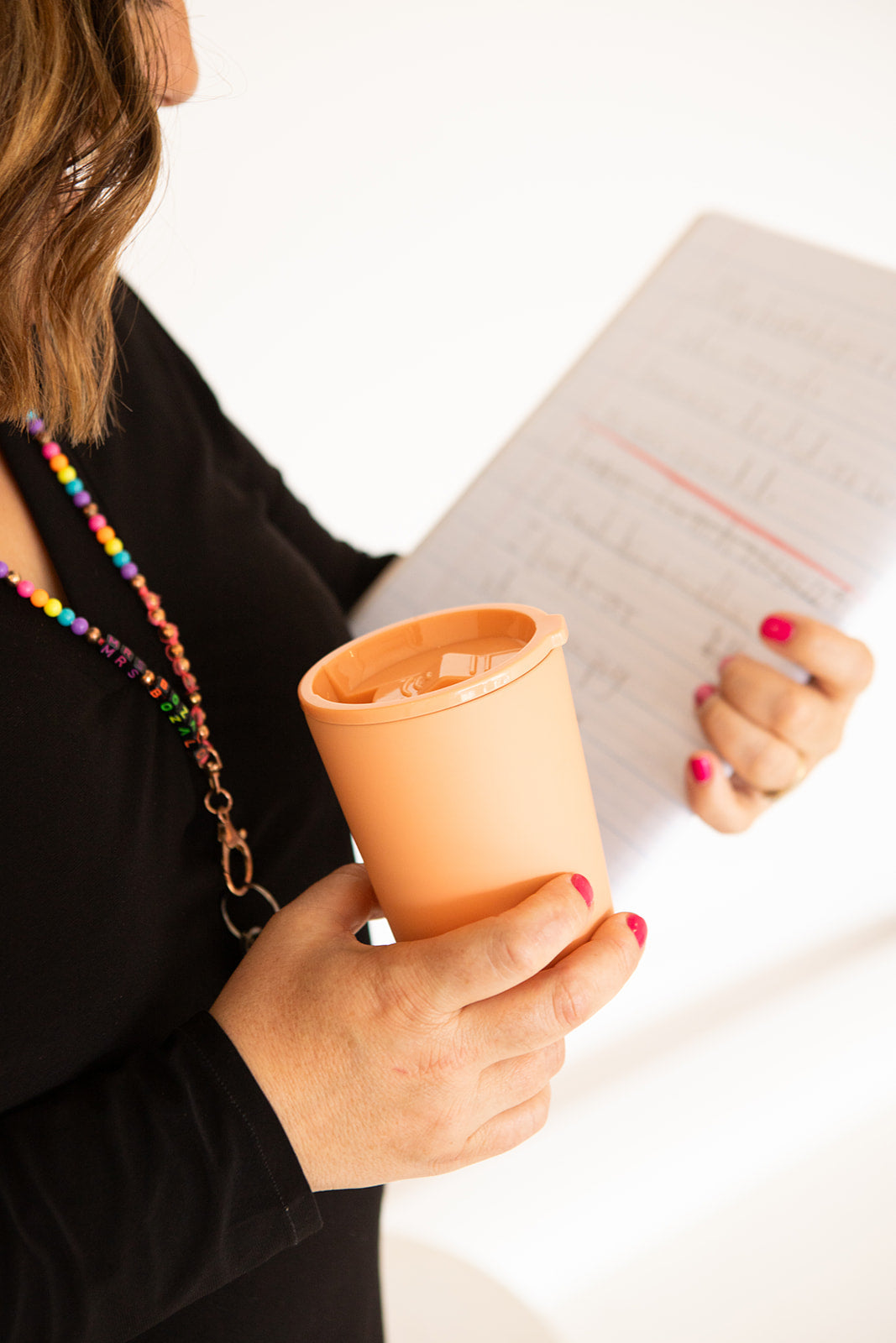 Person holding a peach-colored cup with a notebook on a white background