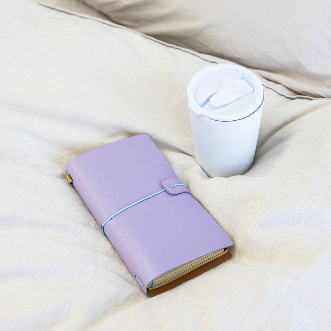 Purple notebook and white tumbler on a bed