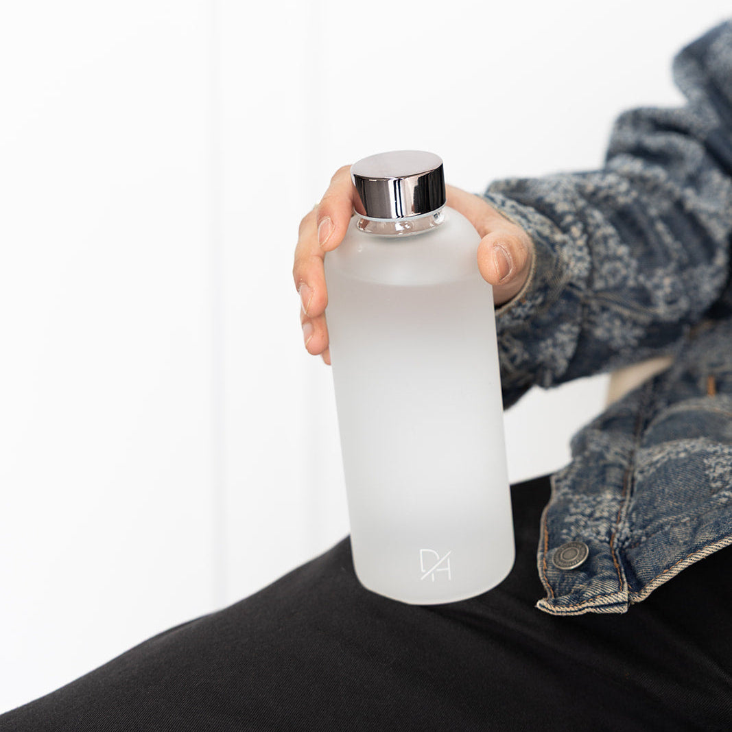 Person holding a clear water bottle with a silver cap on a white background